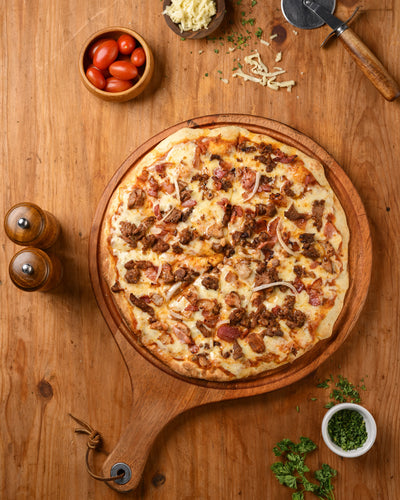 Pizza on a wooden board with ingredients on a wooden table